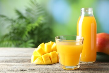 Tasty mango juice in glass, bottle and fresh fruits on wooden table against blurred background, closeup. Space for text