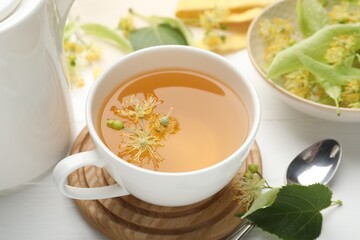 Fresh linden tea in cup and flowers on white wooden table, closeup