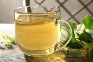 Fresh linden tea in cup and flowers on wooden table, closeup
