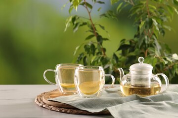 Tasty green tea with lemon in glass cups and teapot on white marble table outdoors