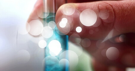 Researcher hand holding small test tube at lab bench, with blue liquid and bokeh overlays