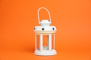 Beautiful white decorative lantern with burning candle on orange background