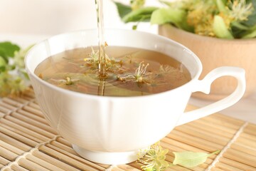 Pouring fresh linden tea into cup and flowers on table, closeup