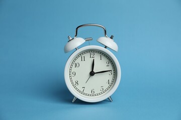 One white alarm clock on light blue background
