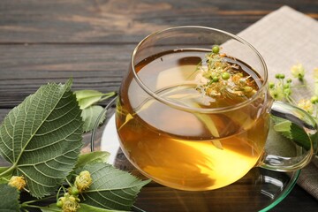 Fresh linden tea in cup and flowers on dark wooden table, closeup