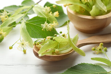 Beautiful linden flowers, leaves, spoon and bowl on white wooden table, closeup