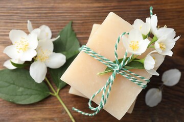 Soap bars and jasmine flowers on wooden table, flat lay