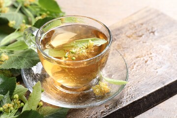 Tasty linden tea in cup, leaves and flowers on table, closeup