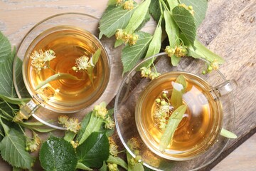 Tasty linden tea in cups, leaves and flowers on wooden table, flat lay