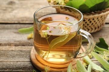 Tasty linden tea in cup, leaves and flowers on wooden table, closeup