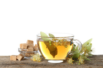 Tasty linden tea in cup, sugar cubes, leaves and flowers on wooden table against white background