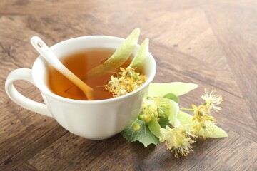 Tasty linden tea in cup, leaves and flowers on wooden table, closeup