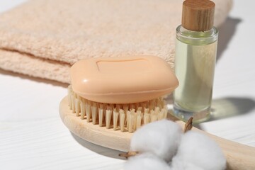 Soap bar, cotton flower, cosmetic product, brush and towel on white wooden table, closeup