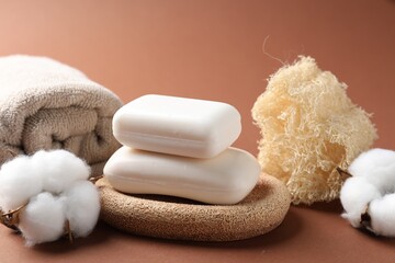 Composition with white soap bars, towel, loofah and cotton flowers on brown background, closeup