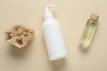 Bottle of liquid soap, loofah and essential oil on beige background, flat lay