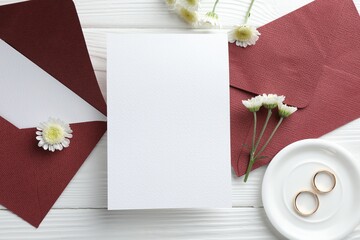 Wedding invitation cards, envelopes, golden rings and flowers on white wooden table, flat lay