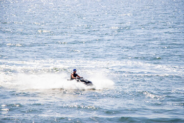 Man riding black jet ski over blue sea with splashing water under bright sunlight. Action shot capturing summer fun and speed on ocean waves. 

