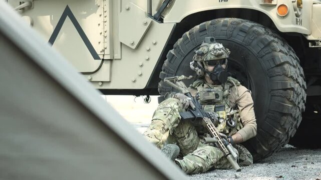 A special forces soldier equipped with a gas mask and advanced combat helmet stands guard by an armored vehicle A concept for CBRN defense and modern warfare readiness
