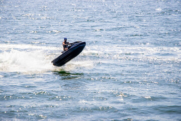 Man riding black jet ski over blue sea with splashing water under bright sunlight. Action shot...