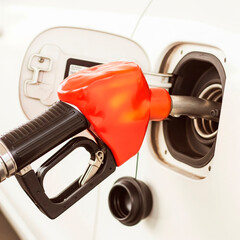 A close-up of a vibrant red fuel pump nozzle at a tank opening, set against a white background with warm colors.