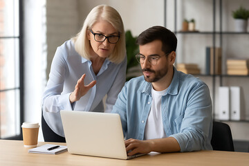 Experienced blonde businesswoman providing valuable assistance and insight to a focused male colleague using a laptop in a modern office environment