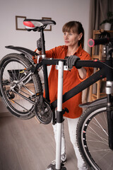 Active cyclist doing bike maintenance routine at home. Middle-aged woman examining damaged bicycle