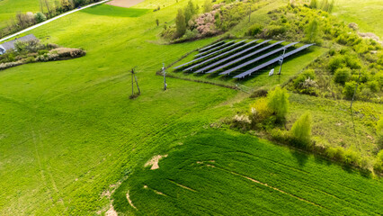 Aerial view of a solar panel installation on a lush green field, emphasizing renewable energy use in rural areas, surrounded by nature and agricultural land.
