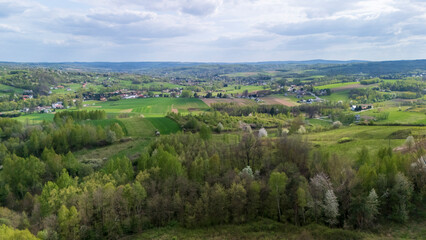 Aerial view of lush green fields and forests under a partly cloudy sky, showcasing the natural beauty of the countryside in spring, inviting outdoor exploration.