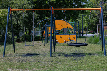 Colorful modern playground with swings and climbing structures on green grass near residential area...