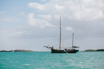 Sailboat drift across turquoise water under cloudy skies in tropical setting