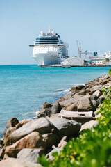 Majestic cruise ship docked at the harbor under clear blue skies beside rocky shoreline on a sunny...