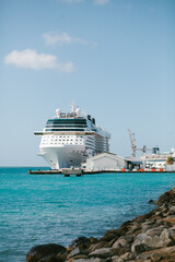 Large cruise ship docked at harbor with vibrant blue waters and rocky shoreline under a clear sky