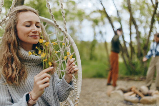 Middle age woman enjoying nature outdoors, holding wildflowers and relaxing in a hammock, promoting active and healthy wellbeing lifestyle in a peaceful forest setting. - Powered by Adobe