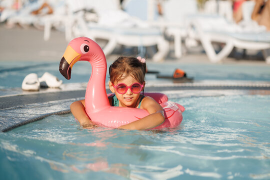 Cute funny toddler girl in a sunglasses relaxing on inflatable toy ring floating in pool have fun during summer vacation. Child having fun in swimming pool.  - Powered by Adobe