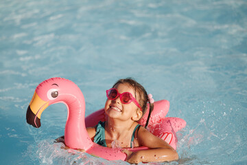 Cute funny toddler girl in a sunglasses relaxing on inflatable toy ring floating in pool have fun during summer vacation. Child having fun in swimming pool. 