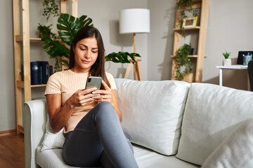 Young woman using smartphone while relaxing on sofa at home