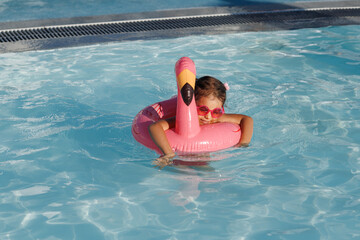 Cute funny toddler girl in a sunglasses relaxing on inflatable toy ring floating in pool have fun...