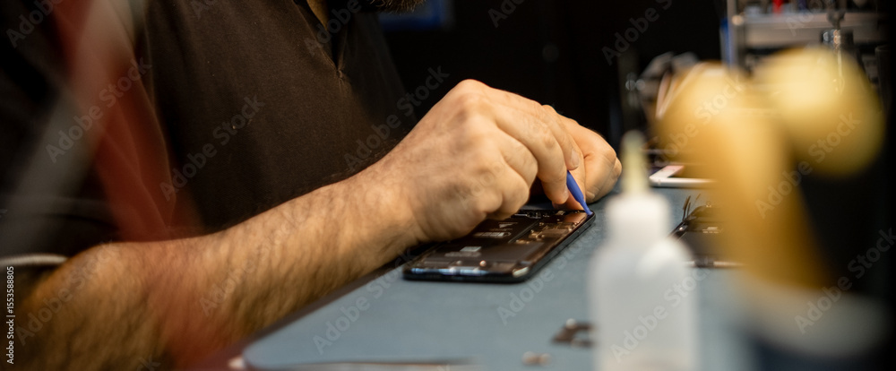 Poster expert technician repairs smartphone with precision in a bustling workshop during the day