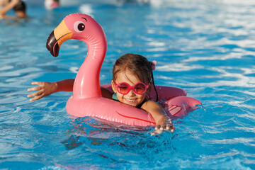 Cute funny toddler girl in a sunglasses relaxing on inflatable toy ring floating in pool have fun during summer vacation. Child having fun in swimming pool. 