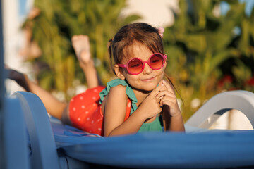 Funny little girl relaxing on summer vacation. The child has fun on the beach. Cute baby in a colorful swimsuit and sunglasses is resting.
