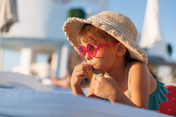 Funny little girl relaxing on summer vacation. The child has fun on the beach. Cute baby in a colorful swimsuit and sunglasses is resting.