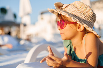 Funny little girl relaxing on summer vacation. The child has fun on the beach. Cute baby in a colorful swimsuit and sunglasses is resting.