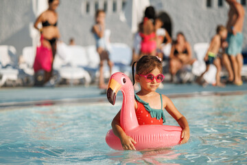 Cute funny toddler girl in a sunglasses relaxing on inflatable toy ring floating in pool have fun during summer vacation. Child having fun in swimming pool. 