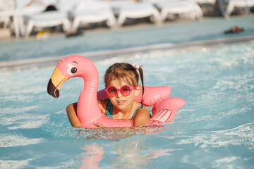 Cute funny toddler girl in a sunglasses relaxing on inflatable toy ring floating in pool have fun during summer vacation. Child having fun in swimming pool. 