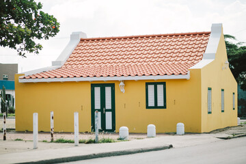 Colorful yellow house with red roof and green shutters in a sunny tropical environment © tisaeff