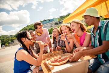 A diverse group of young friends enjoying pizza together outdoors, celebrating a sunny summer day under vibrant umbrellas