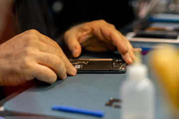 Phone Repair Technician Works Meticulously on a Device at a Bustling Repair Shop in Late Afternoon