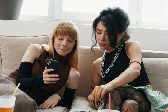 two young adult women socializing and working together as colleagues in a modern workplace, sharing ideas and using a smartphone actively