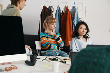 young adult woman and colleagues socializing at workplace, relaxed coworkers discussing business in...