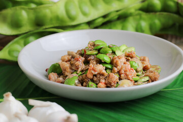 close up of spicy thai stir fried sator with shrimp and minced pork served in white bowl with fresh sator pods and garlic on green banana leaf traditional southern thai cuisine for food lovers